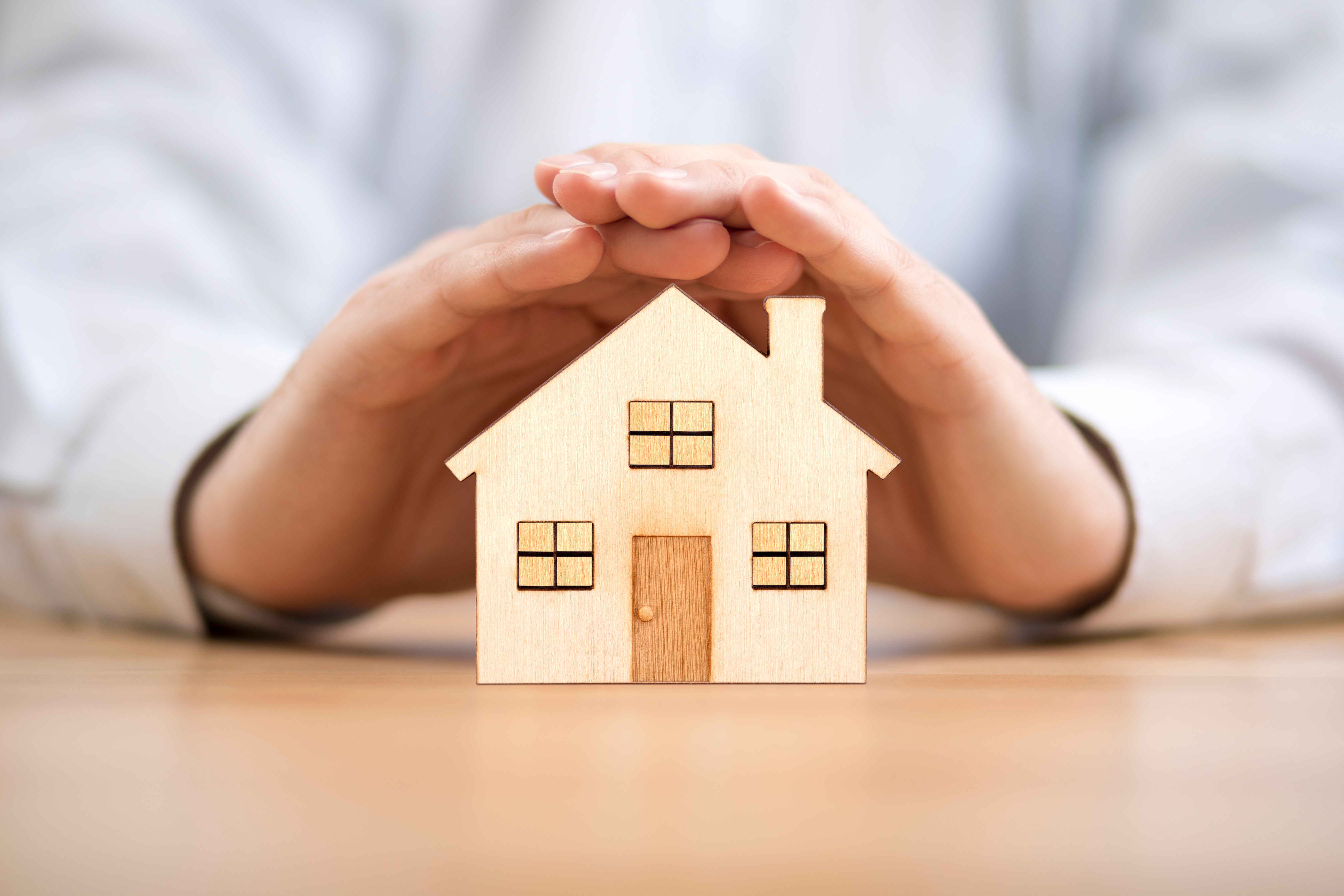 Hands protectively cupping a small wooden house model, symbolizing homeowners insurance coverage