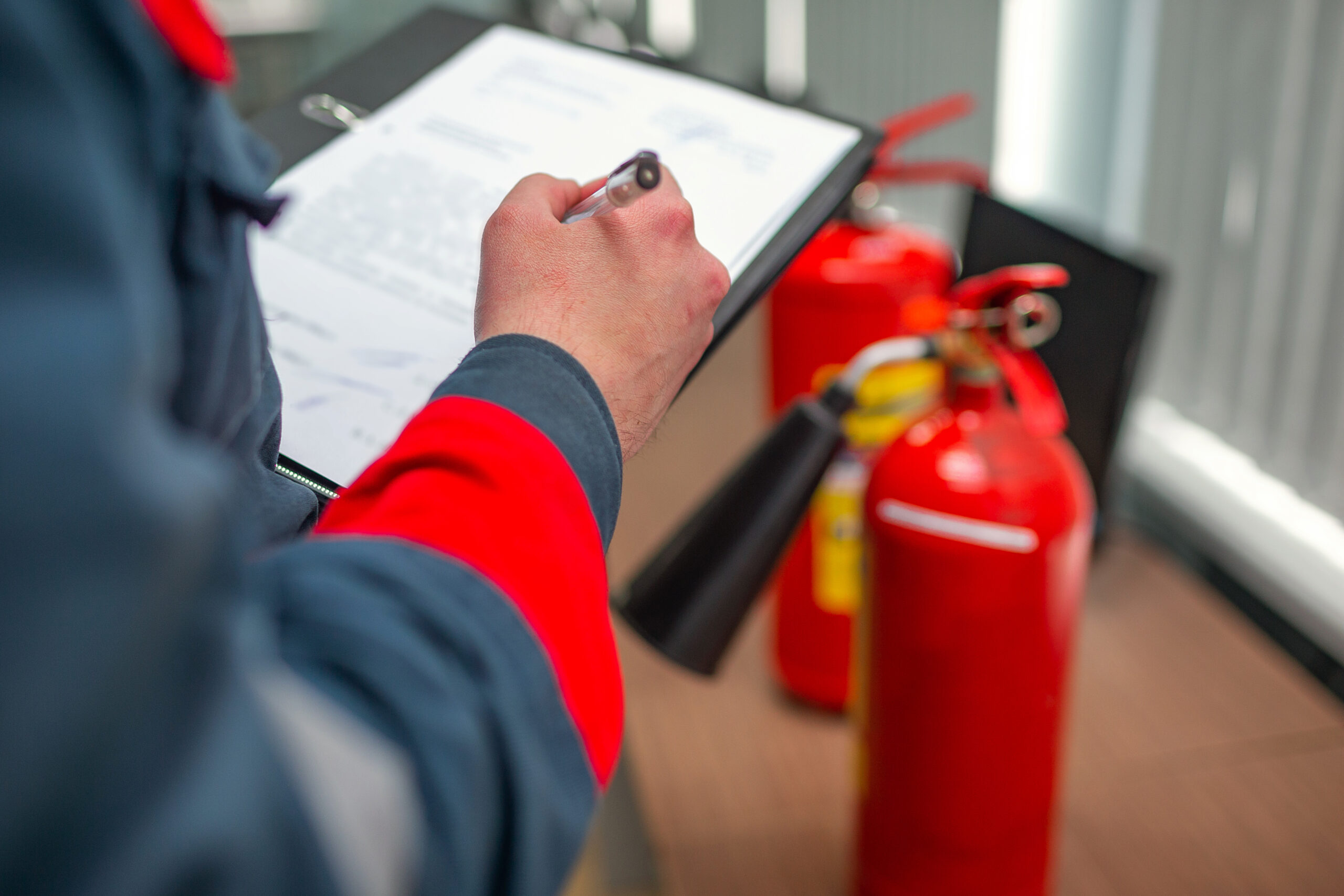 Inspector with clipboard examining fire extinguishers, highlighting importance of fire insurance compliance