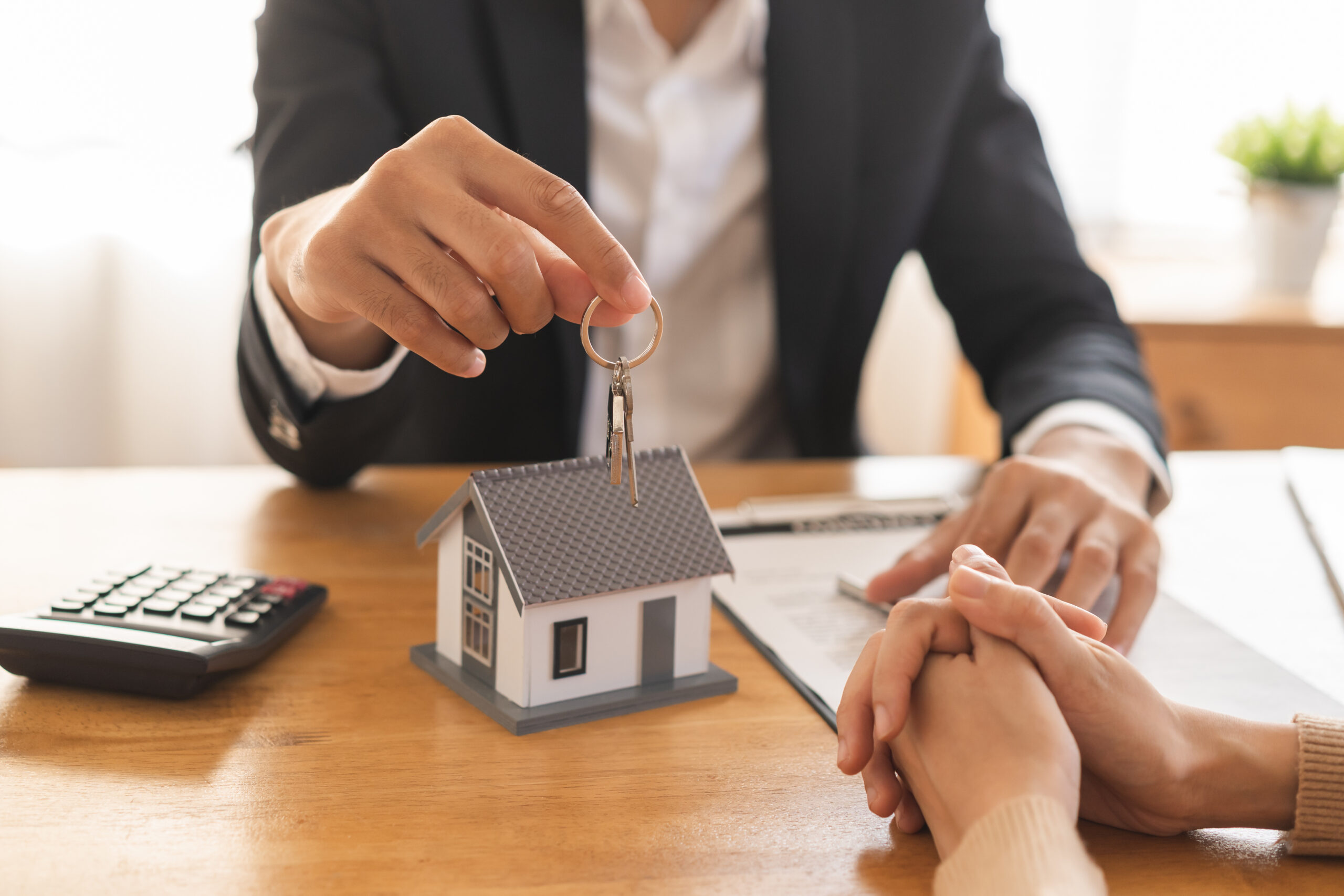 real estate agent holding house key model, discussing home insurance options with client