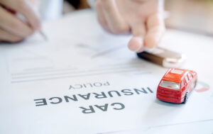 Close-up of hands filling out car insurance policy, with toy car symbolizing potential impact on car insurance premium.